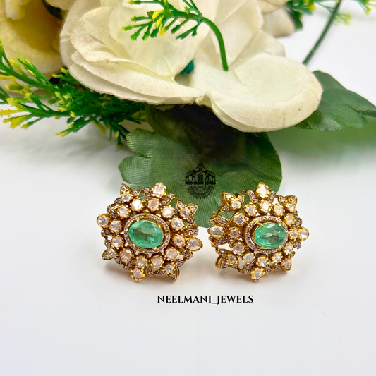 Gold earrings with green gemstones on a white background with flowers.