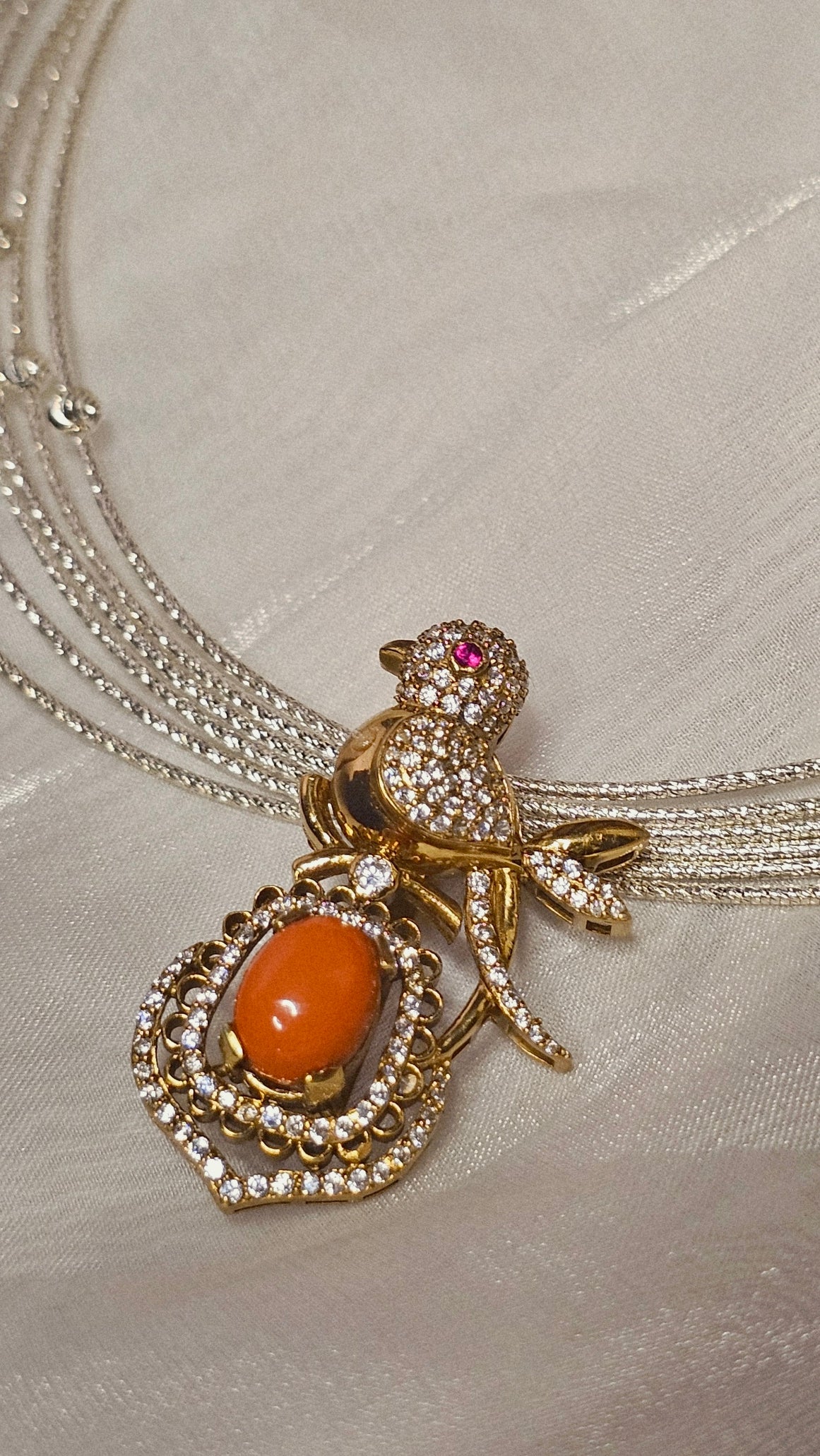 Gold and diamond bird pendant necklace with orange gemstone on cream fabric