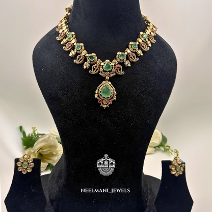 Necklace with green gemstones on a black mannequin bust, accompanied by earrings, with Neelamani Jewels branding.