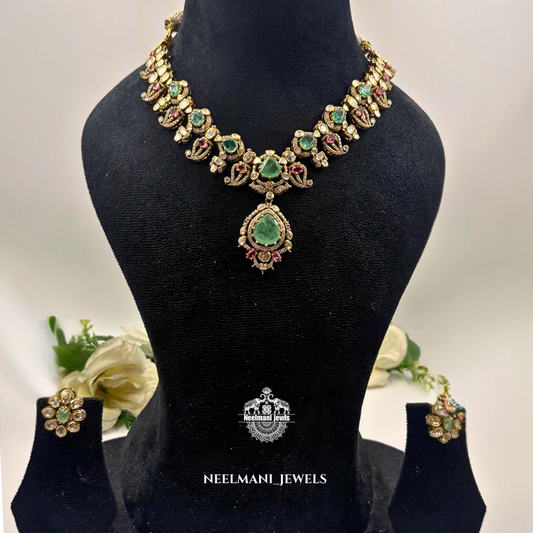Necklace with green gemstones on a black mannequin bust, accompanied by earrings, with Neelamani Jewels branding.
