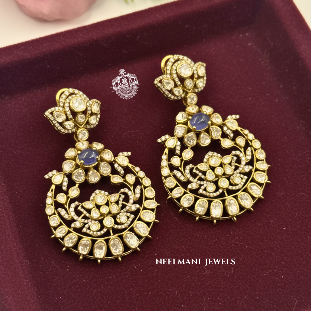 Gold earrings with blue stones on a maroon cushion, branded 'Neelmani Jewels'.