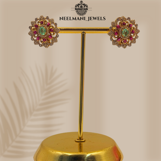 Gold earrings with gemstones on a gold stand, branded 'Neelmani Jewels'.