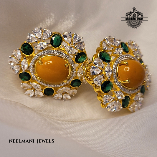 Gold earrings with green and orange stones on a beige fabric background, branded 'Neelmani Jewels'.